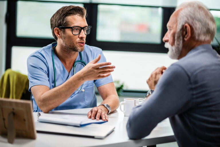 General practitioner consulting mature man during medical appointment at doctor's office.