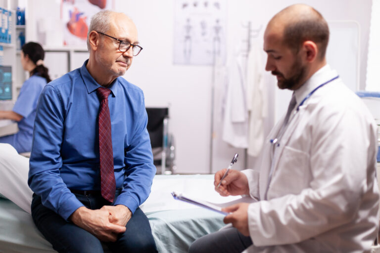 Surgeon wearing stethoscope discussing treatment in examination room with senior man. Elderly patient having a converstation with medical stuff in private clinic during consultation.
